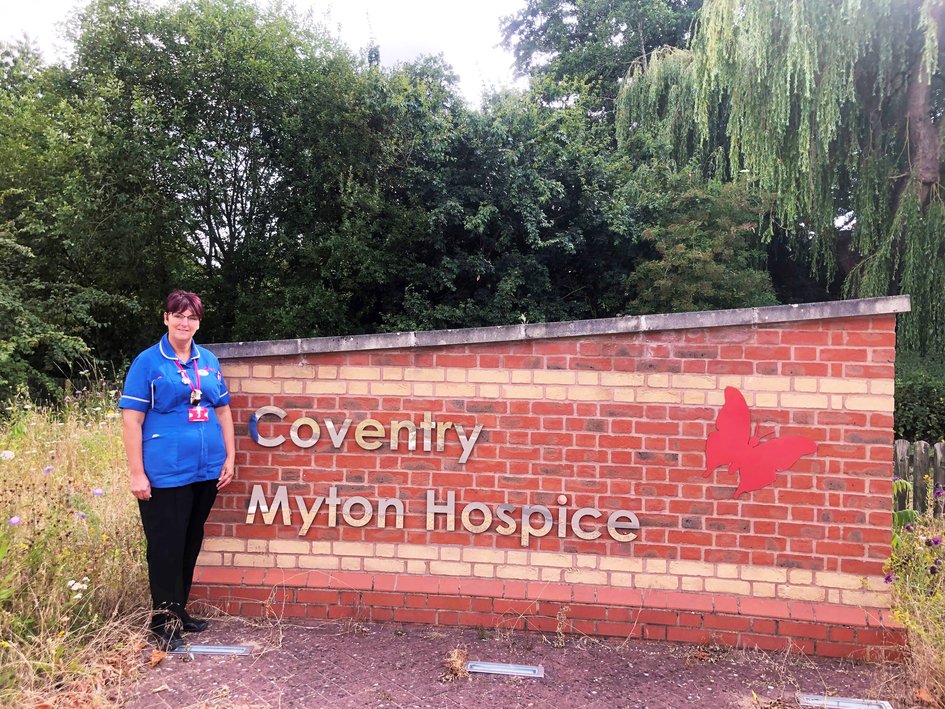 Kerry Merry in front of Coventry Myton Hospice Sign